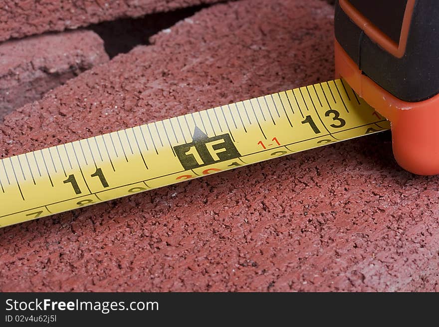 Orange tape measure on a red brick.