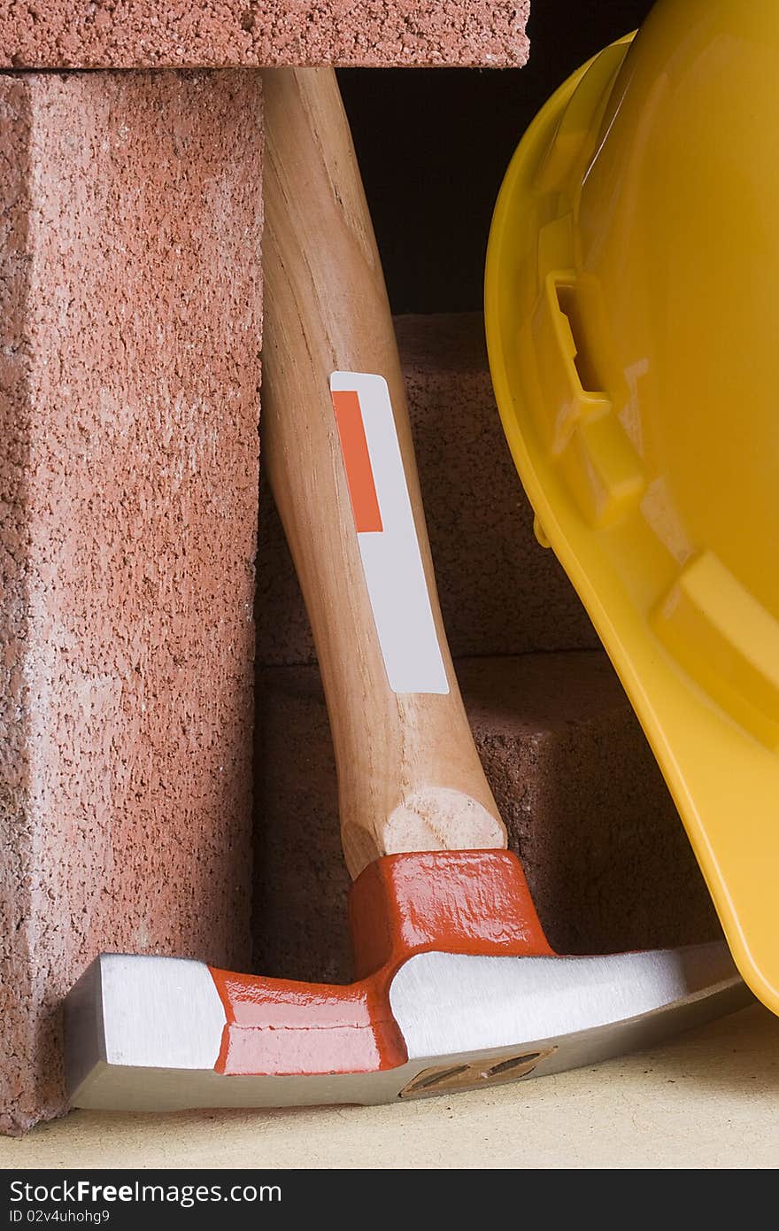 Stonemason's hammer next to red bricks and a yellow hard hat.