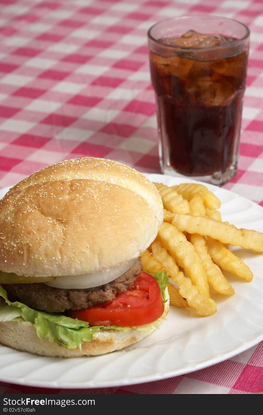 A freshly cooked hamburger and fries meal on a checkered tablecloth. A freshly cooked hamburger and fries meal on a checkered tablecloth.