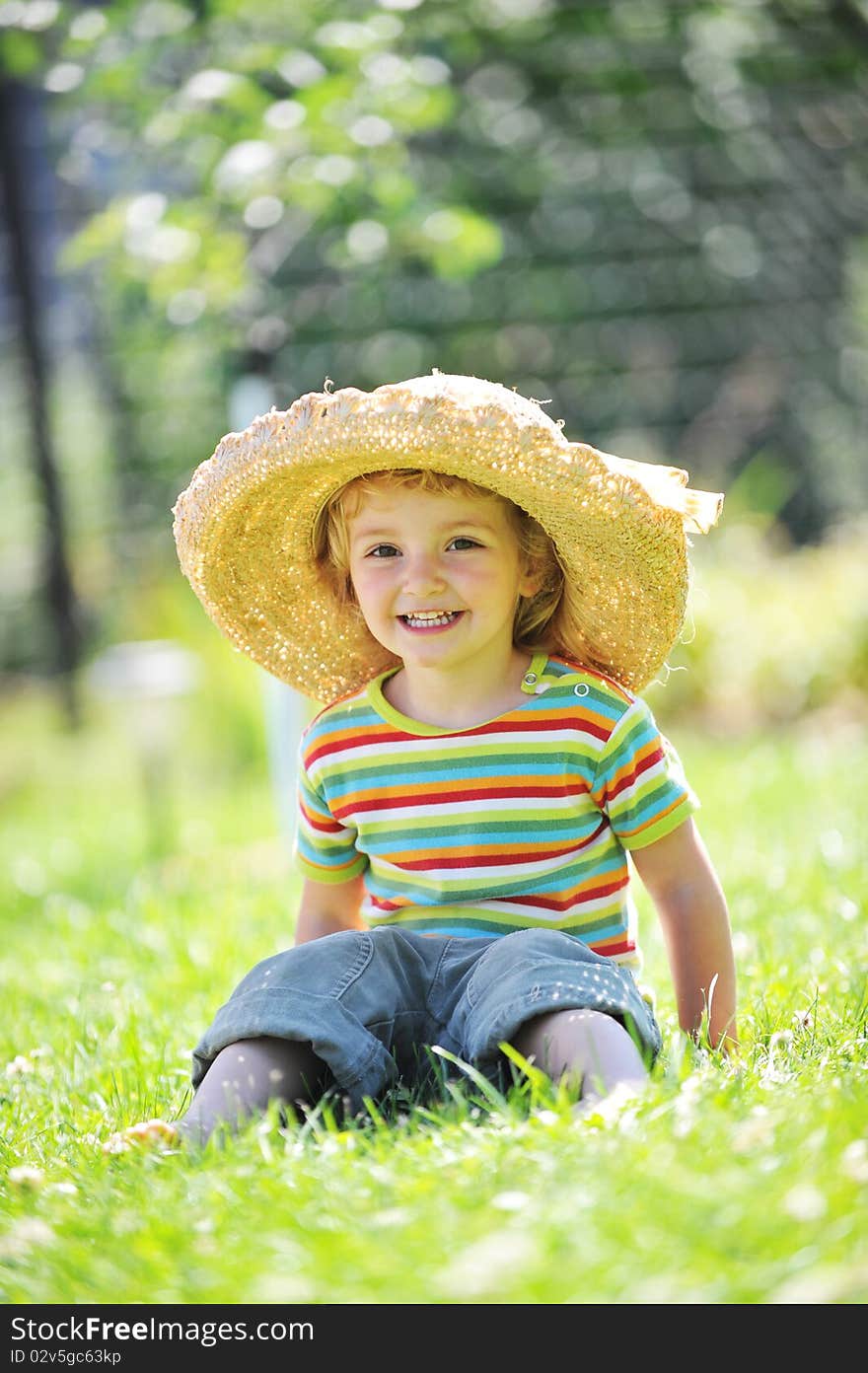 Little girl in straw hat sitting on green grass