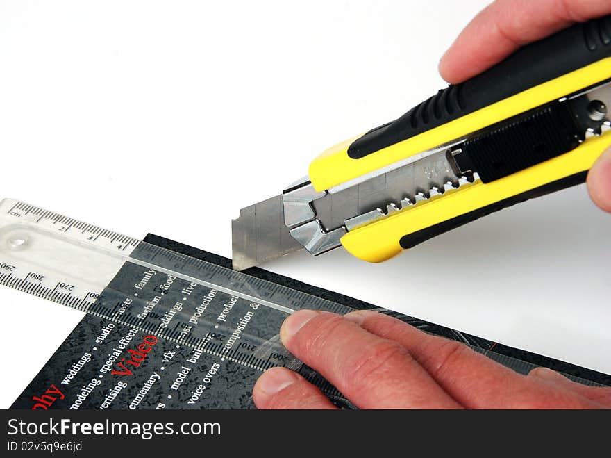 A yelow and black craft knife cutting through black and red cardboard. A yelow and black craft knife cutting through black and red cardboard