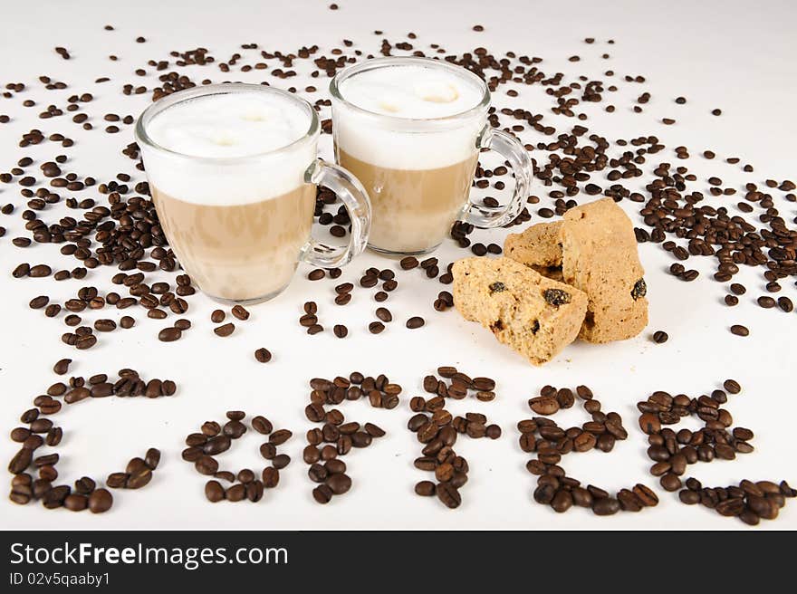 Two cups of freshly brewed latte macchiato standing between some coffee beans, and with a couple of rusks.