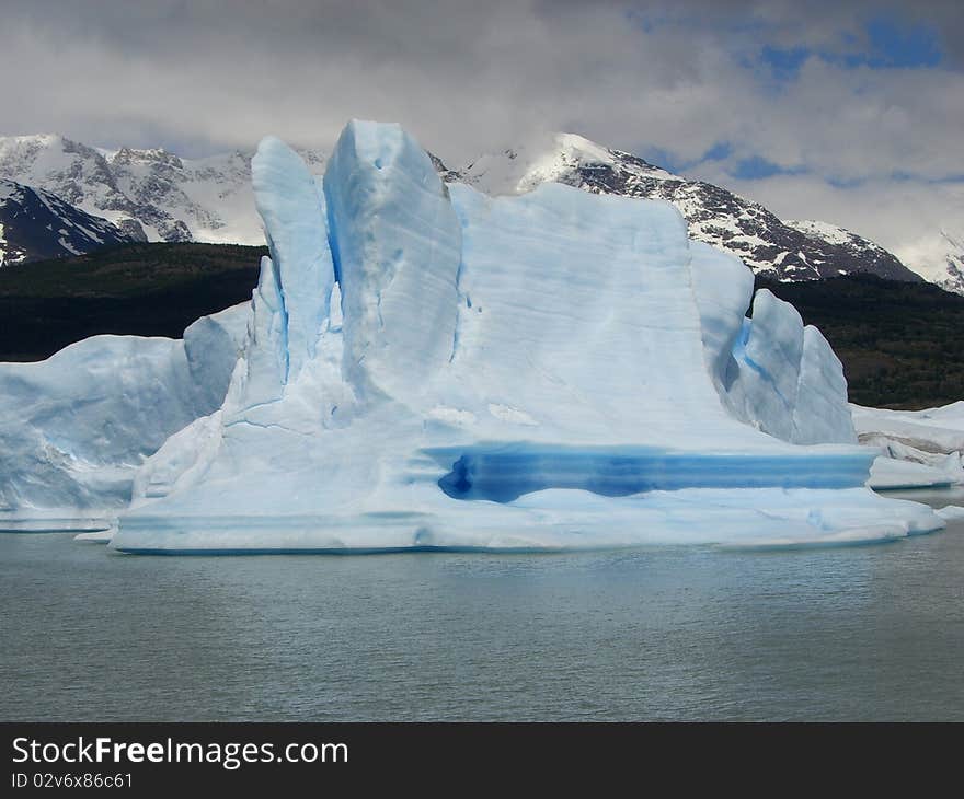 Iceberg floating in the water with mountain backdrop