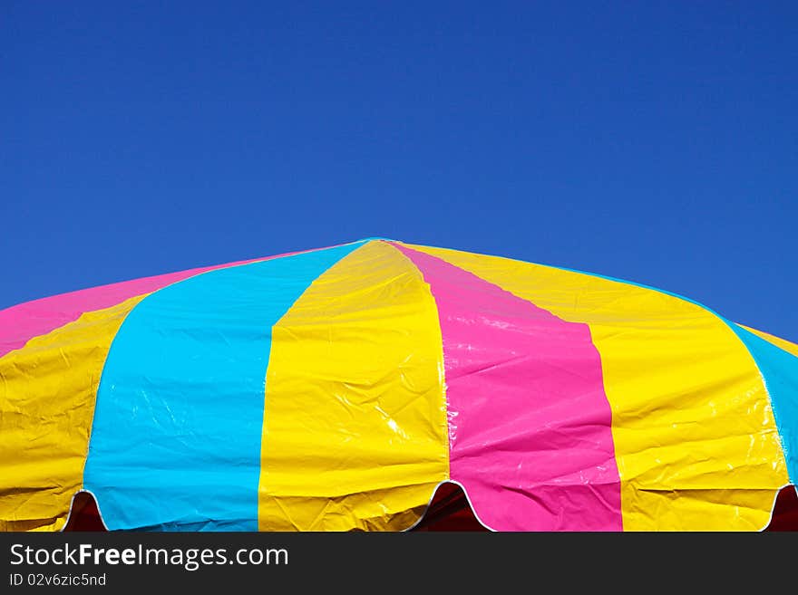 Multi-colored umbrella against a bright blue sky; with copy space for text