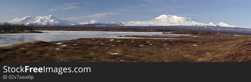 Panorama with volcanos, tundra, and the river covered by an ice. Russia. Kamchatka. Panorama with volcanos, tundra, and the river covered by an ice. Russia. Kamchatka.