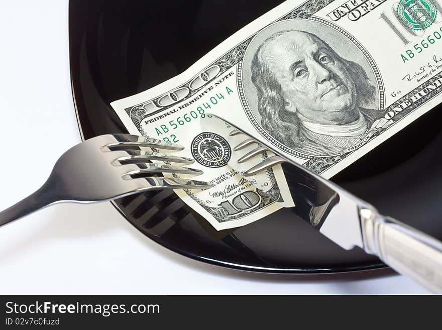 Banknote on a black plate with knife and fork