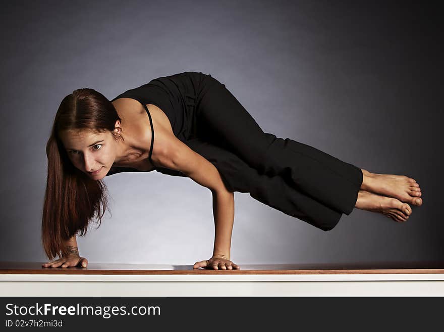 Young lady practicing sideways crow yoga posture (Ashtavakrasana) in black clothes on grey background, low-key image. Young lady practicing sideways crow yoga posture (Ashtavakrasana) in black clothes on grey background, low-key image.