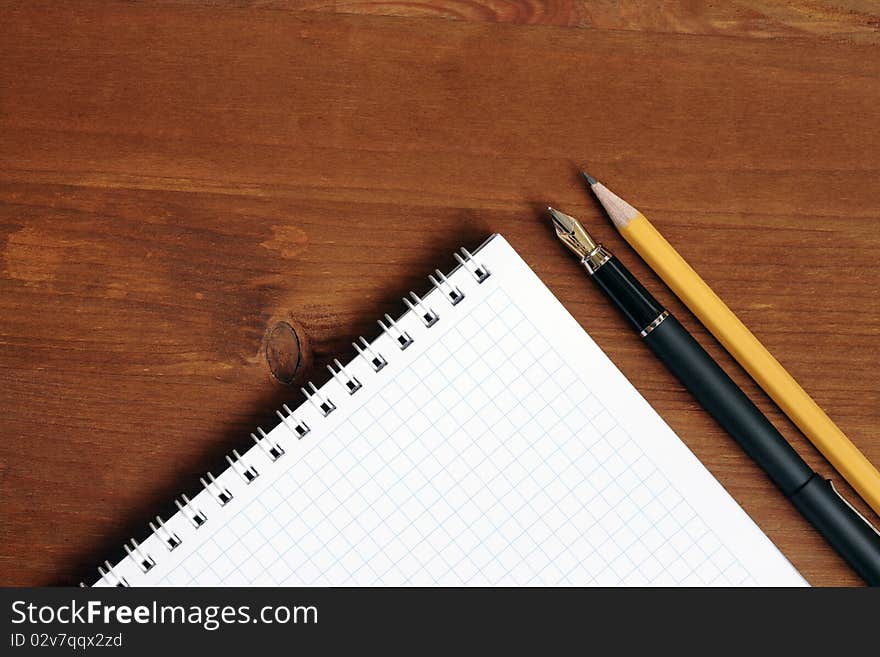 Closeup of blank spiral notebook near pen and pencil on wooden table. Closeup of blank spiral notebook near pen and pencil on wooden table