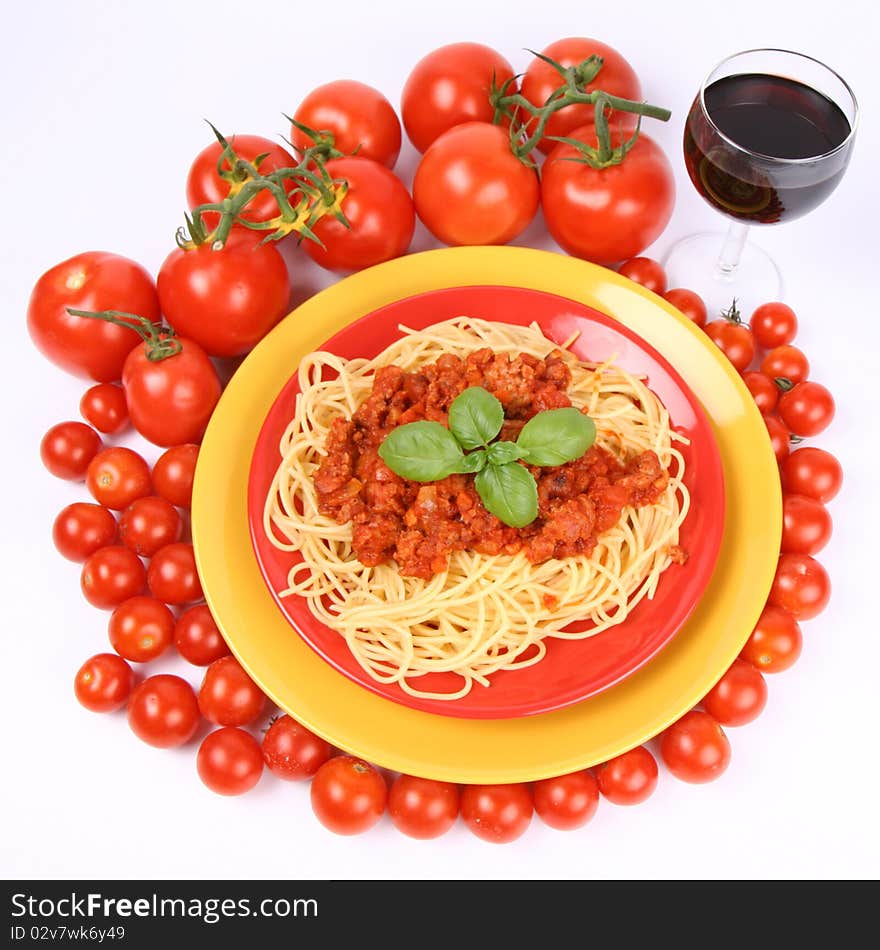 Spaghetti Bolognese on a plate decorated with fresh basil, some tomatoes and cherry tomatoes, and a glass of red wine