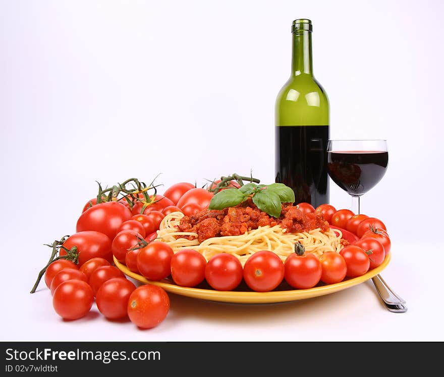 Spaghetti Bolognese on a plate decorated with fresh basil and surrounded with tomatoes and cherry tomatoes, and some red wine