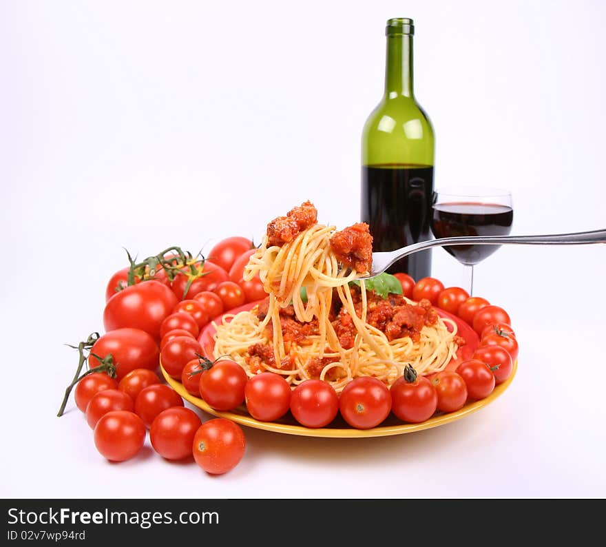 Spaghetti Bolognese being eaten with a fork from a plate, decorated with fresh basil, some regular tomatoes and cherry tomatoes, and some red wine