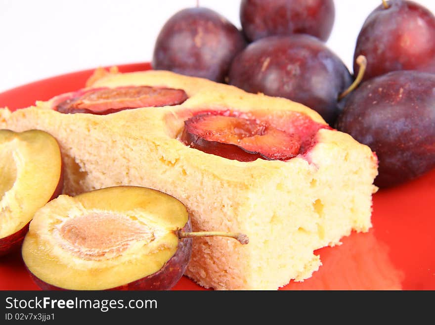 Portion of a Plum Pie and some fresh plums on a red plate