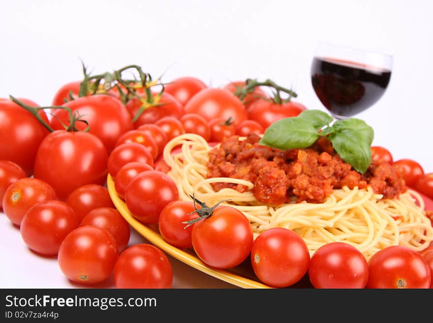 Spaghetti Bolognese on a plate decorated with fresh basil, some tomatoes and cherry tomatoes, and a glass of red wine