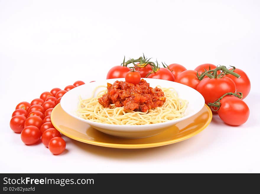 Spaghetti Bolognese on a plate decorated with fresh basil and surrounded with tomatoes and cherry tomatoes on white background