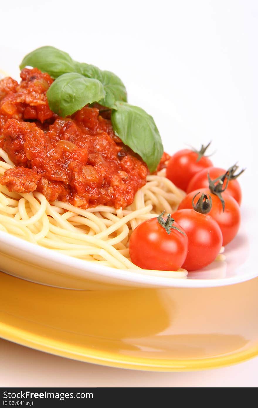 Spaghetti Bolognese on a plate decorated with fresh basil and cherry tomatoes in close up