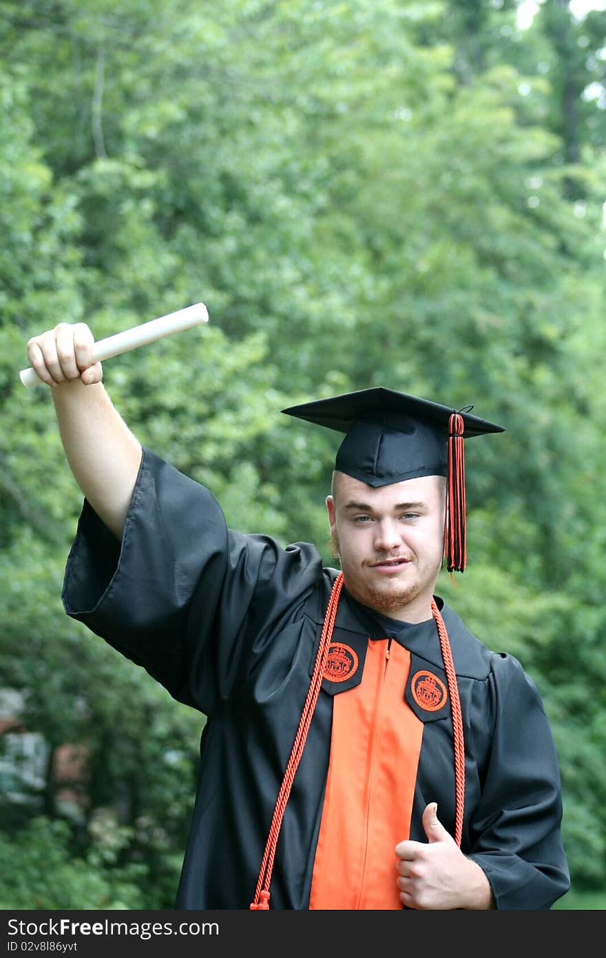 Young man in cap and gown holding diploma in air, graduating from college. Young man in cap and gown holding diploma in air, graduating from college