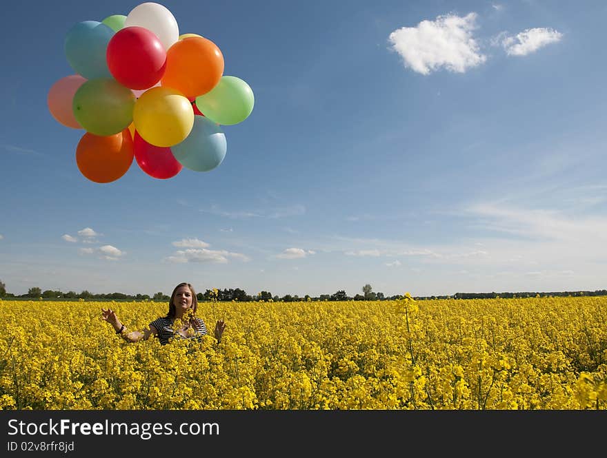 Girl with colorful balloons in canola field