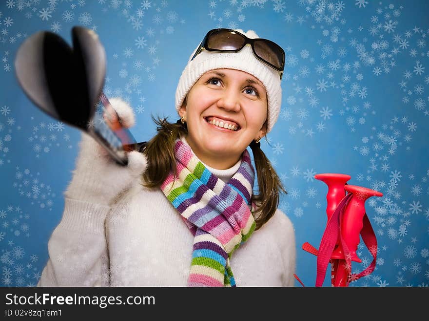 Portrait the beautiful woman in a cap with ski sticks in hands on a blue background. Portrait the beautiful woman in a cap with ski sticks in hands on a blue background