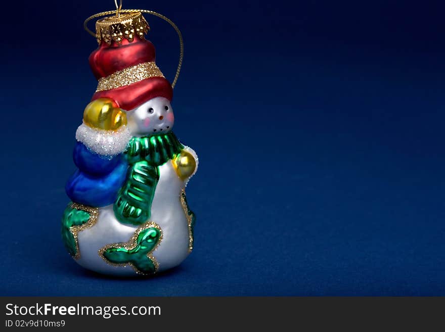 Closeup of a glass snowman ornament on blue background.