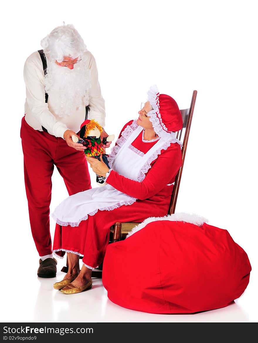 Mr. and Mrs. Santa Clause admiring a doll before putting it into Santa's sack. Isolated on white. Mr. and Mrs. Santa Clause admiring a doll before putting it into Santa's sack. Isolated on white.