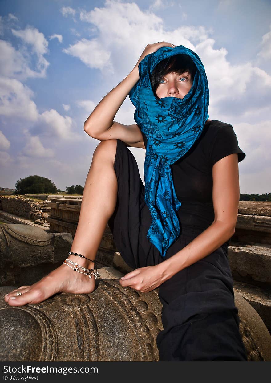 Woman in blue kerchief sits on stone sculpture. Woman in blue kerchief sits on stone sculpture