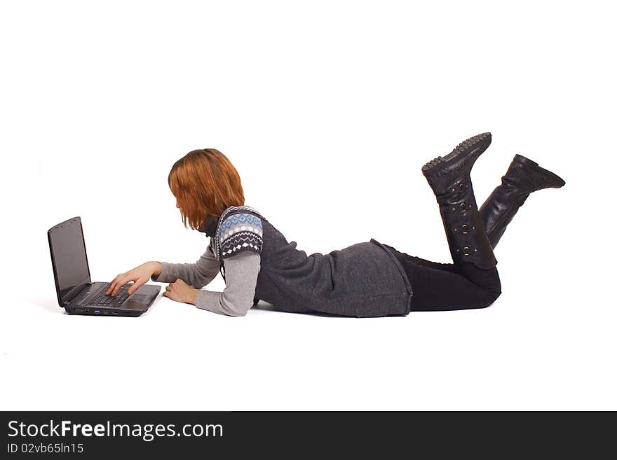 Young beautiful girl in knit dress lying and looking at laptop, isolated on white