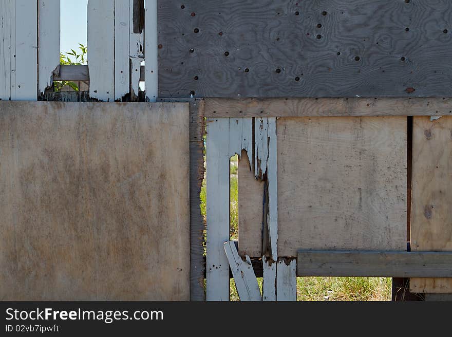 A heavily repaired wooden plank fence around industry area. You can just see a few leaves and some grass through the holes of the fence. A heavily repaired wooden plank fence around industry area. You can just see a few leaves and some grass through the holes of the fence.