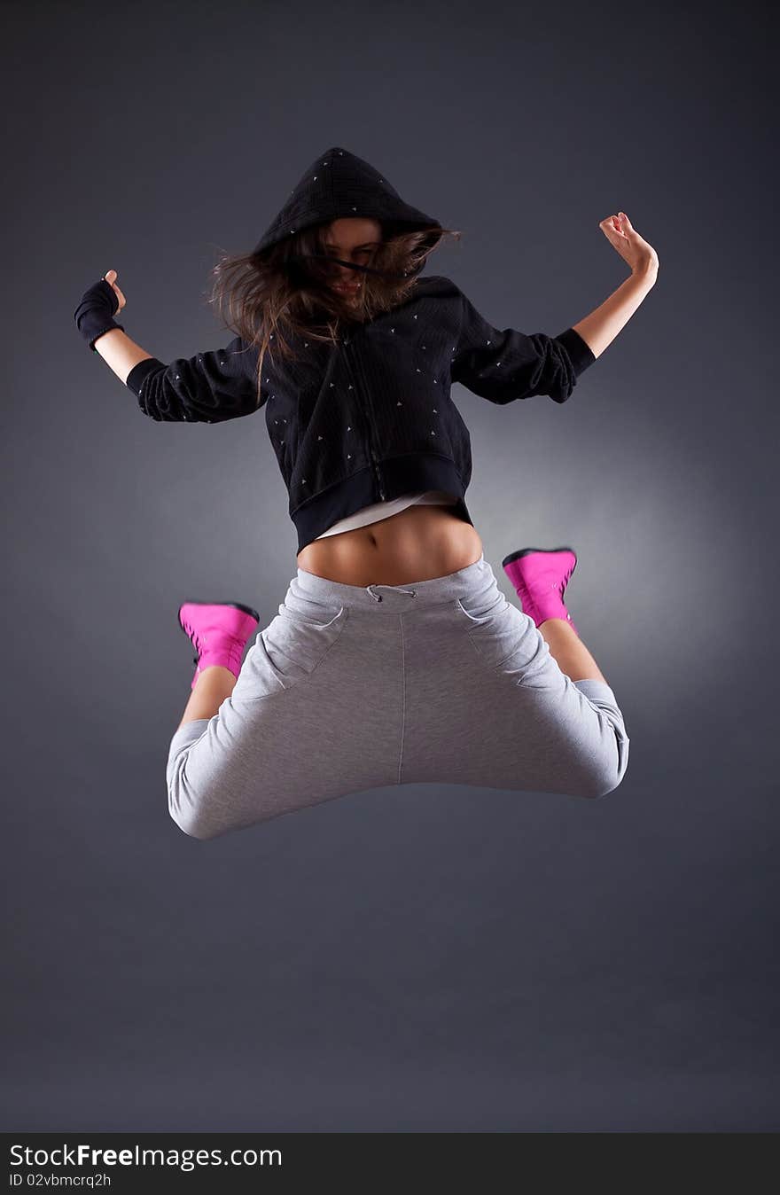 Young female dancer jumping on the grey background