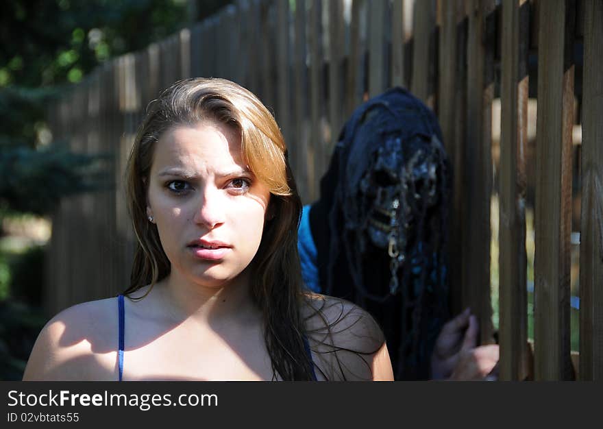 A girl stands with scared look while a man stands behind her with a scary mask. A girl stands with scared look while a man stands behind her with a scary mask.