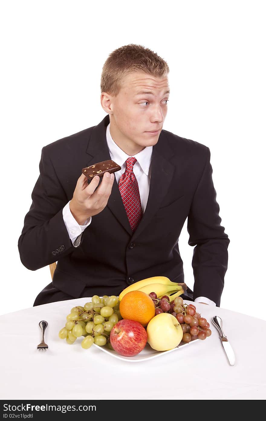 A man sneaking a brownie and looking over his shoulder when he should be eating his plate.