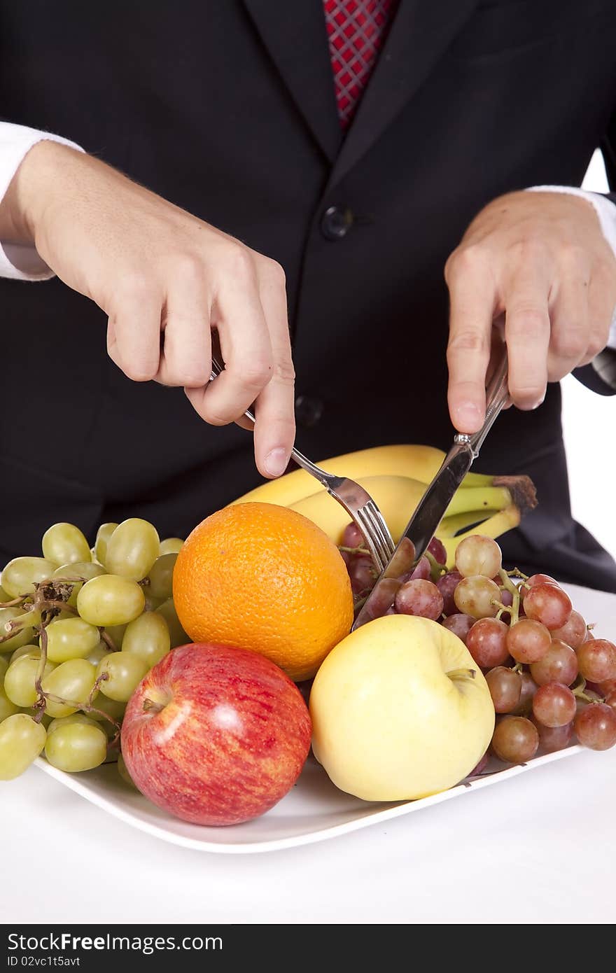 A close up view of a man holding his fork and knife getting ready to dig into a plate of fruit. A close up view of a man holding his fork and knife getting ready to dig into a plate of fruit.