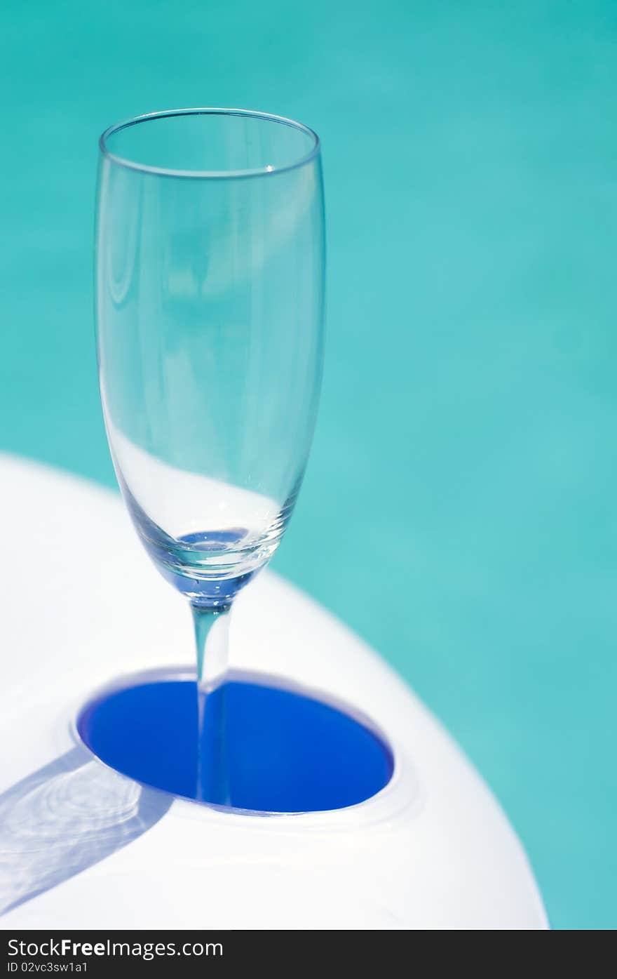 Empty fizz glass in rubber inflatable pool table with azure water in background. Empty fizz glass in rubber inflatable pool table with azure water in background