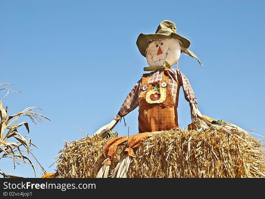 A fall scarecrow sitting on a bail of hay with blue sky background, copy space. A fall scarecrow sitting on a bail of hay with blue sky background, copy space