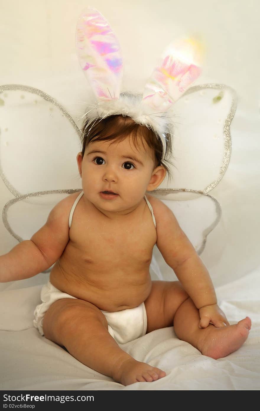 Cute baby sitting and smiling with angel wings and colorful bunny ears