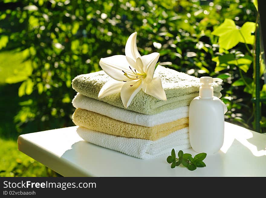 Backloghting with sun white lily on stack of towels against green summer background. Backloghting with sun white lily on stack of towels against green summer background