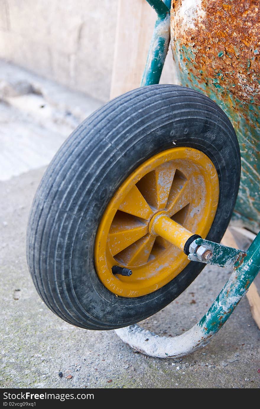 The wheel of an old wheelbarrow leaning against a wall of a house under construction during a break