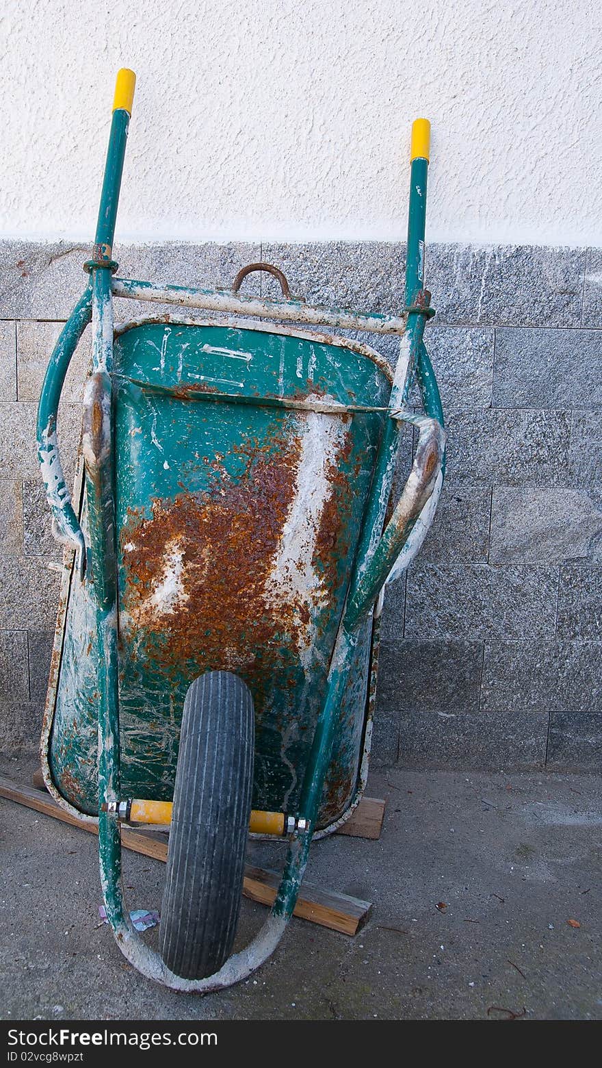 An old wheelbarrow leaning against a wall of a house under construction during a break