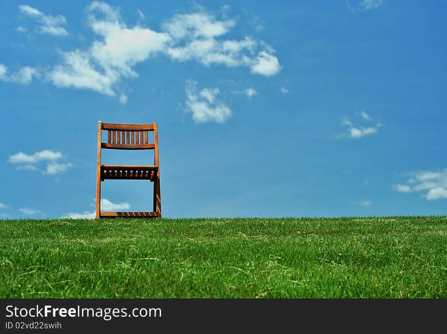 A Wooden chair with grass and sky. A Wooden chair with grass and sky