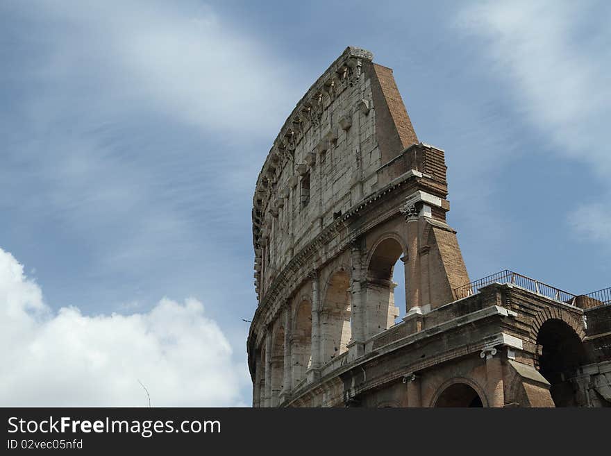 Daytime image of the Roman Coliseum with bright sun and partly cloudy skys.