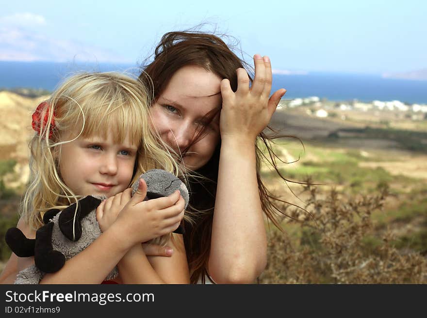 Beautiful woman embracing a little girl on sea summer background. Beautiful woman embracing a little girl on sea summer background