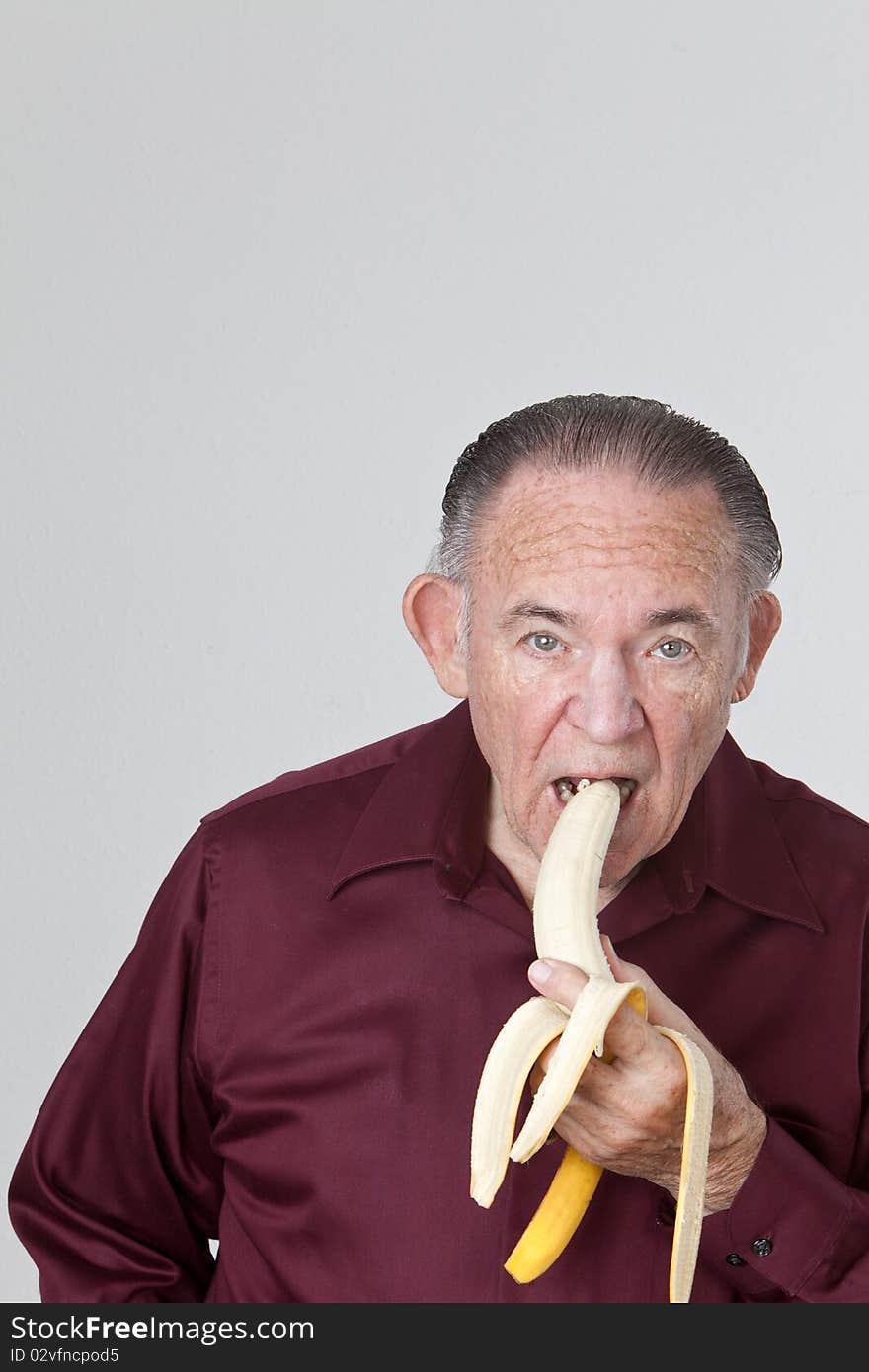 Mature man wearing a maroon shirt and eating a banana. Mature man wearing a maroon shirt and eating a banana.