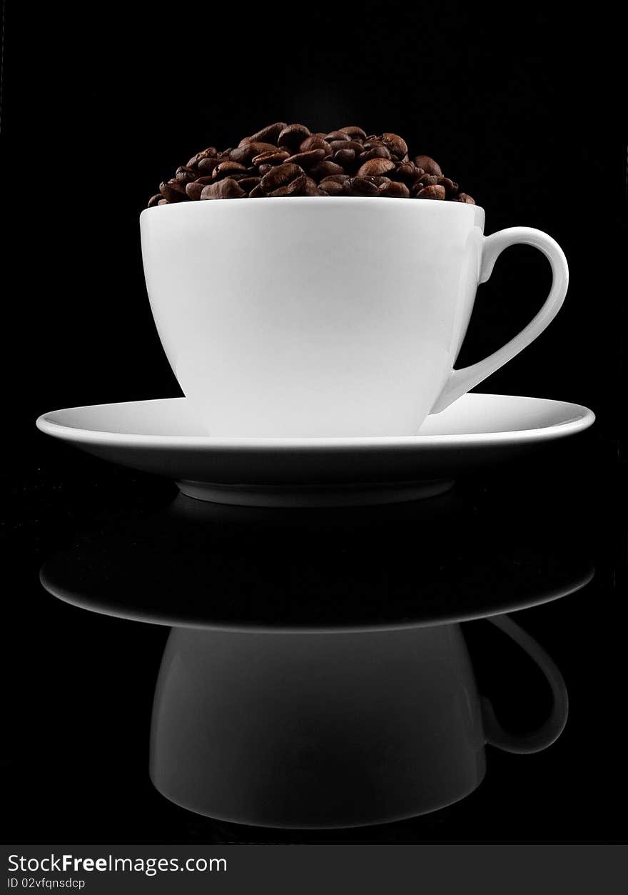 Cup of coffee with coffee beans inside placed on black reflective background