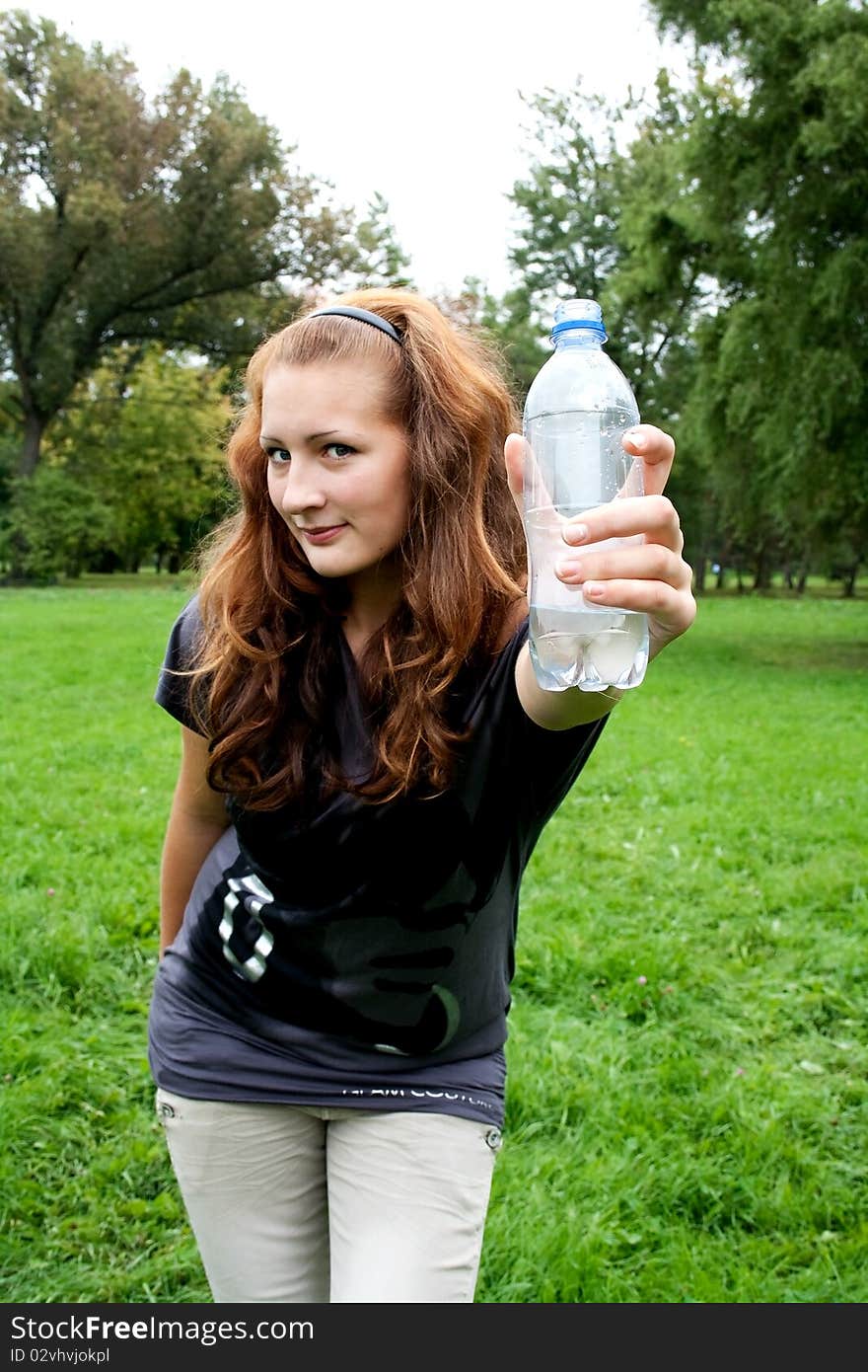 Girl on the background of fresh greens holding out a bottle of water. Girl on the background of fresh greens holding out a bottle of water