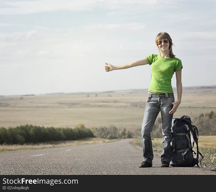 Young smiling woman with backpack catching a car on empty road