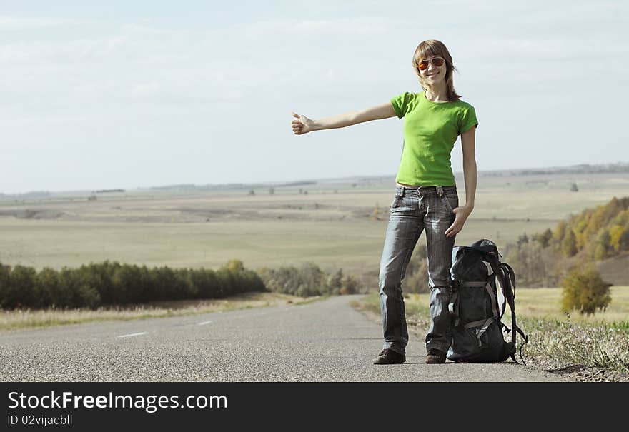 Young smiling woman with backpack catching a car on empty road