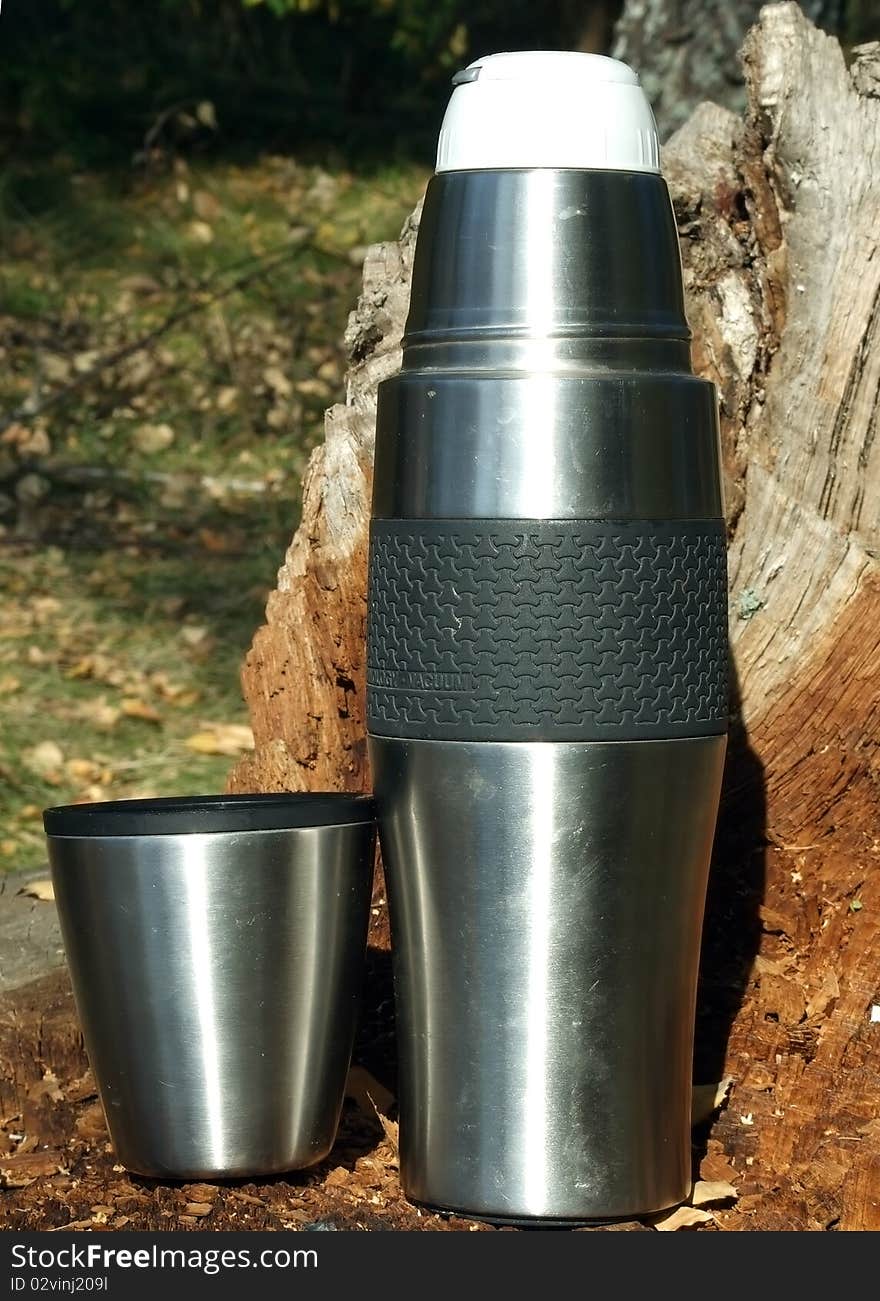 Vacuum flask and a glass on an old stump of a tree at a picnic