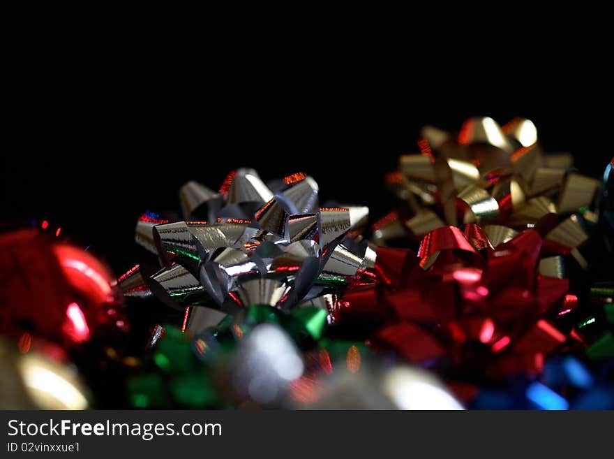 Holiday bows on a black background.  Narrow depth of field, main focus on silver bow.  Reflections on bows from colored holiday lights. Holiday bows on a black background.  Narrow depth of field, main focus on silver bow.  Reflections on bows from colored holiday lights.