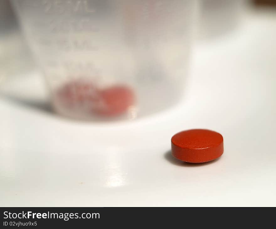 Close up shot of red tablet and medicine cup in background