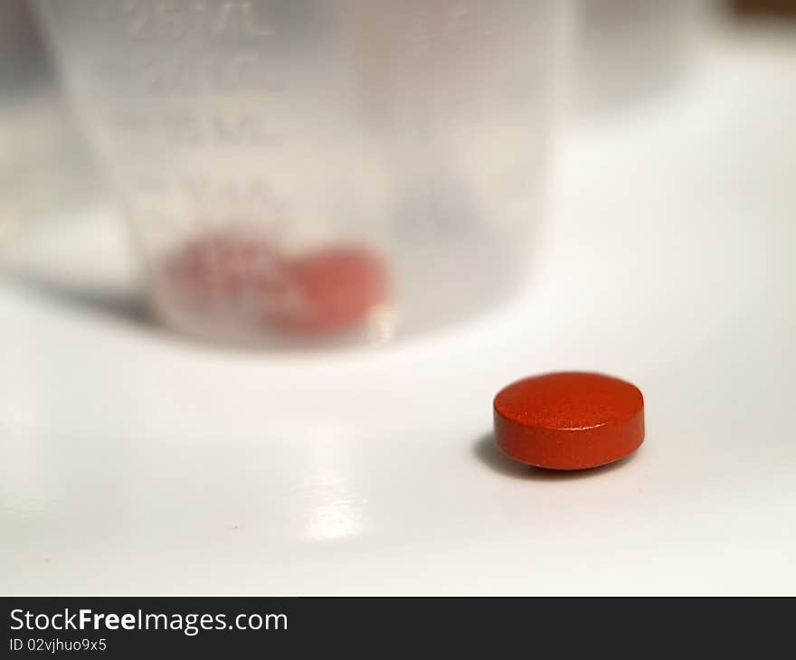 Close up shot of red tablet and medicine cup