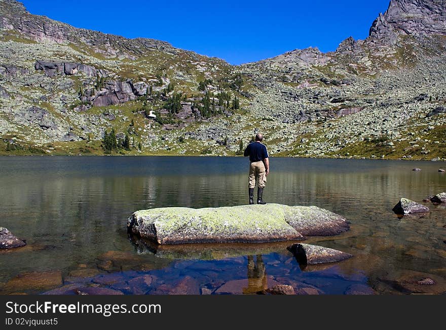 Man costs on a stone and looks at mountains.